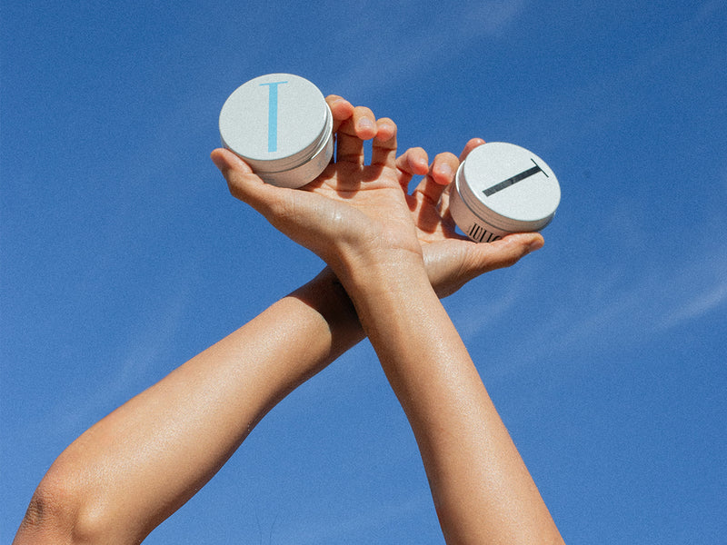 Two Tuttofare tallow balm jars, Roman Blue and Holy Grail, against a blue sky